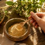 Une main prélève délicatement de la poudre de maca, baignée par la lumière du jour.